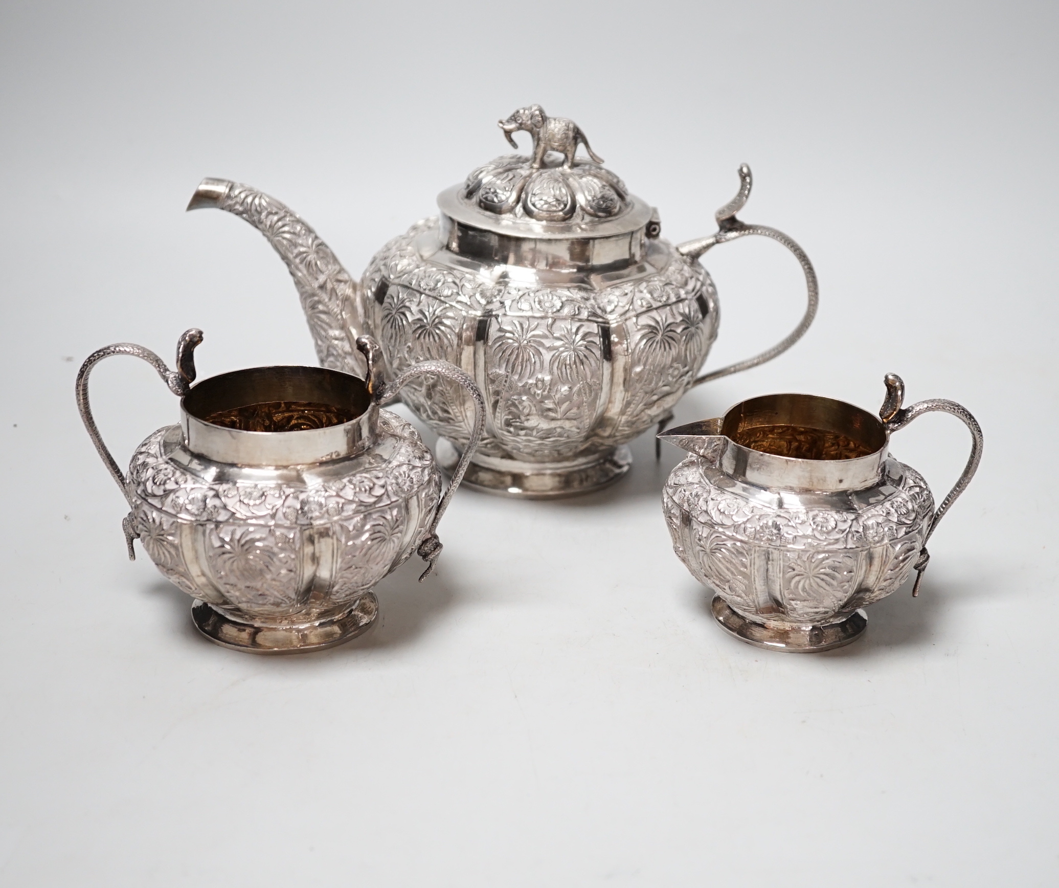An Indian embossed white metal three piece tea set, with cobra handles and elephant finial, 25.7oz.